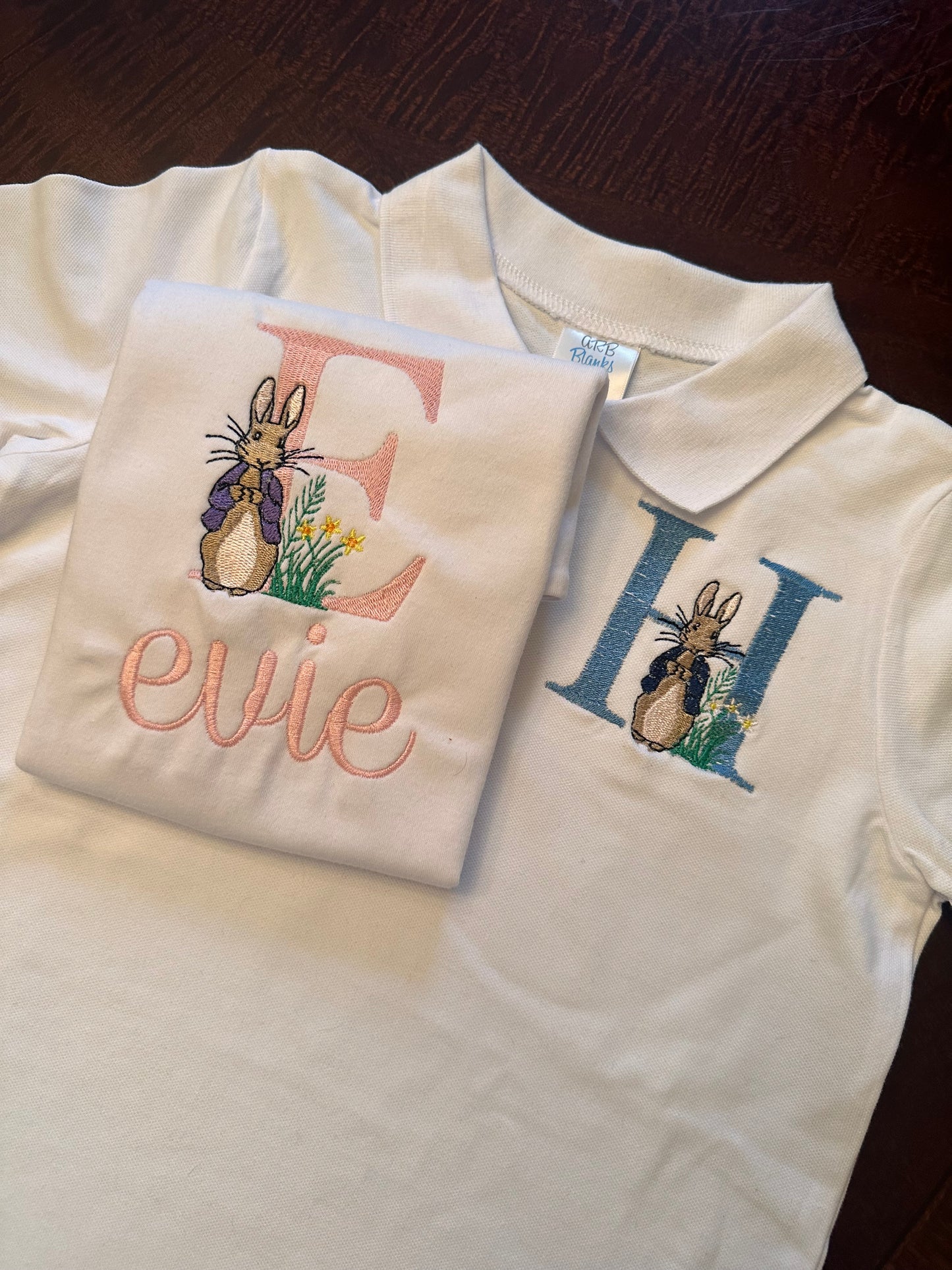 Set of personalized Easter shirts for kids featuring embroidered Peter Rabbit design with custom initials and names β girls shirt with pink 'E' and name 'Evie', boys polo with blue 'H', perfect for Easter outfits and spring celebrations.