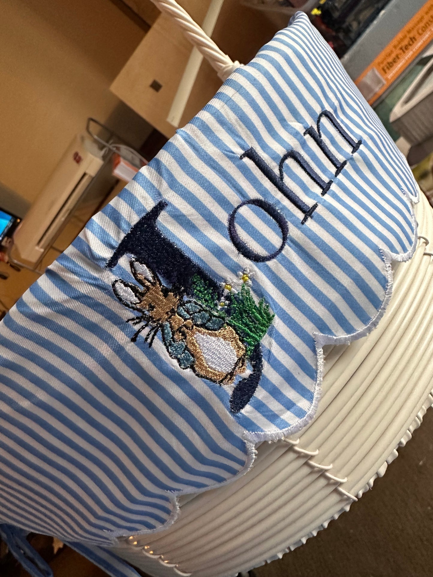 Custom embroidered Easter basket liner with Peter Rabbit design and personalized name 'John' in navy thread on blue and white striped fabric, featuring scalloped white trim – handmade Easter basket insert for kids.