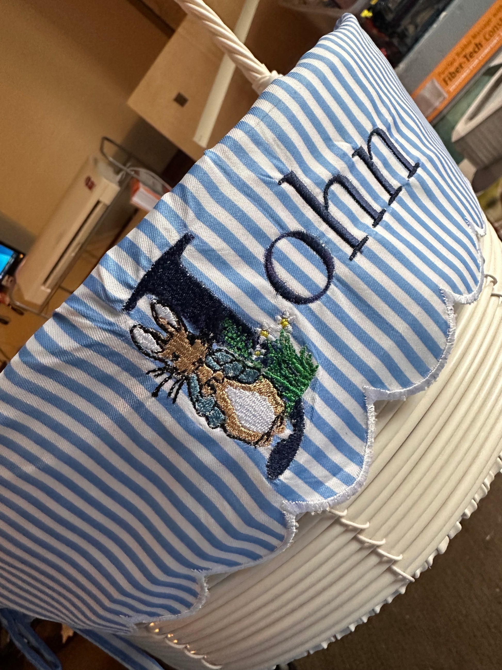 Custom embroidered Easter basket liner with Peter Rabbit design and personalized name 'John' in navy thread on blue and white striped fabric, featuring scalloped white trim – handmade Easter basket insert for kids.