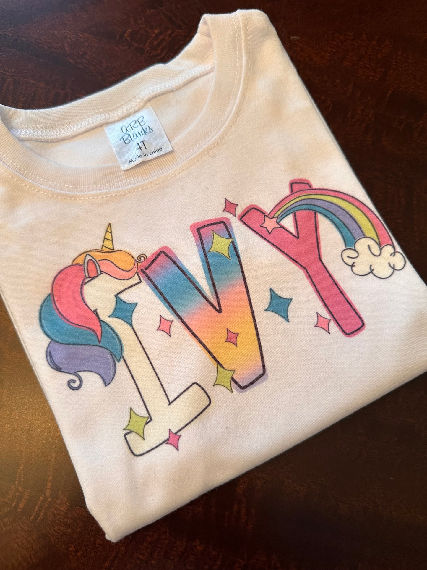 Personalized unicorn shirt for kids featuring a custom name in colorful rainbow gradient letters with unicorn and star accents, perfect for birthdays, parties, or everyday wear.