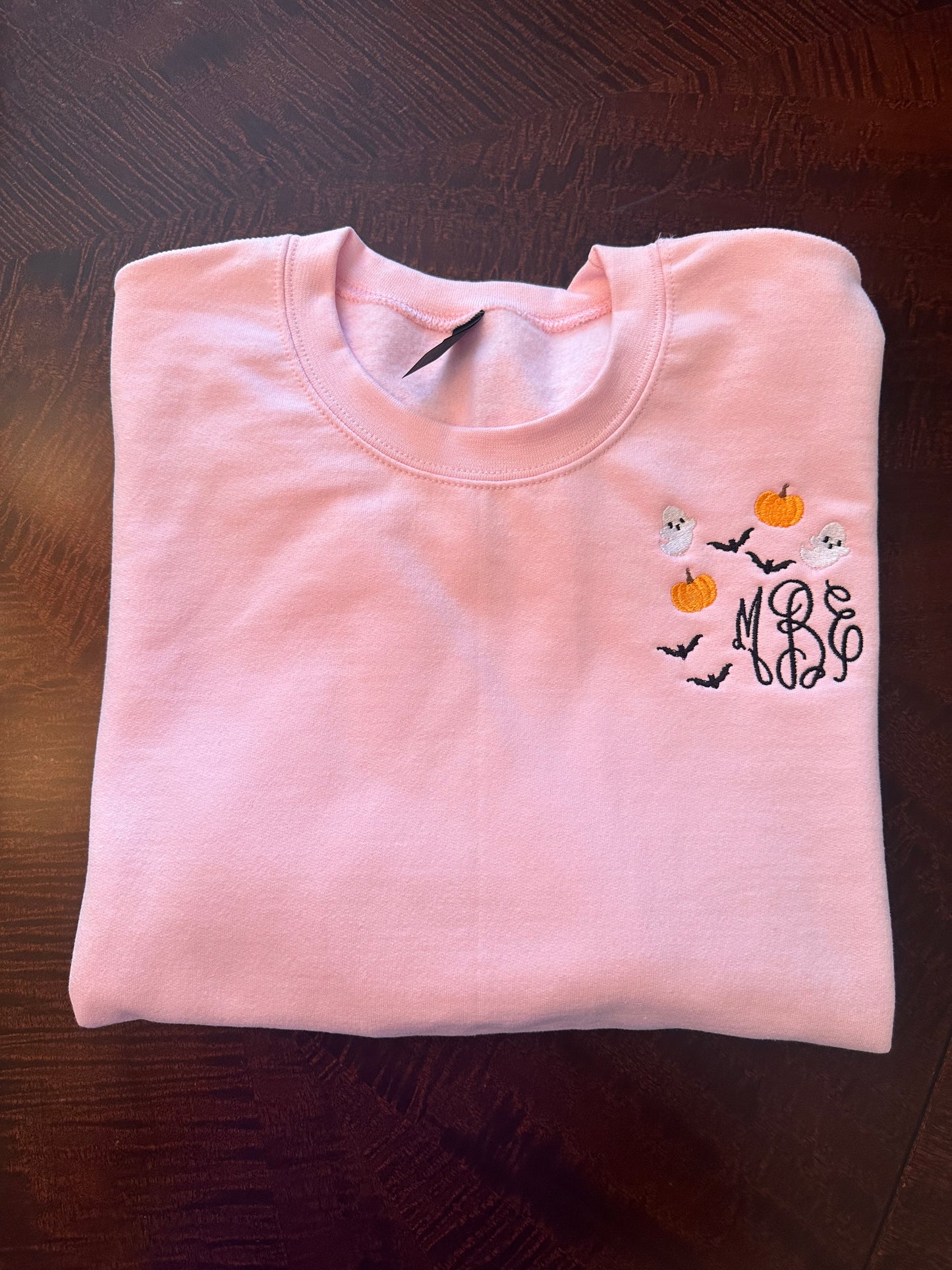 Folded pink embroidered sweatshirt with monogram and ghost-pumpkin embroidery — personalized spooky season crewneck