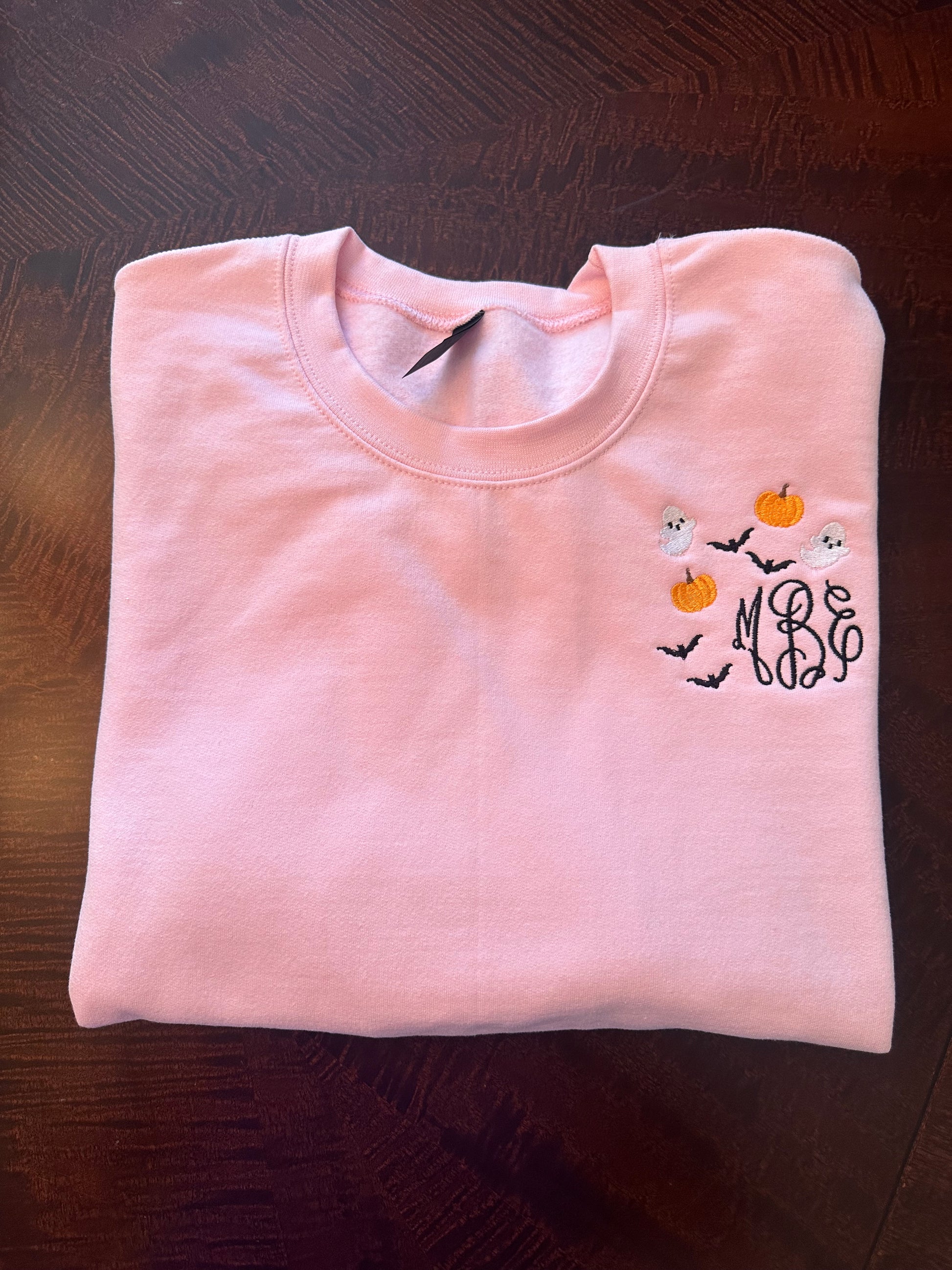 Folded pink embroidered sweatshirt with monogram and ghost-pumpkin embroidery — personalized spooky season crewneck