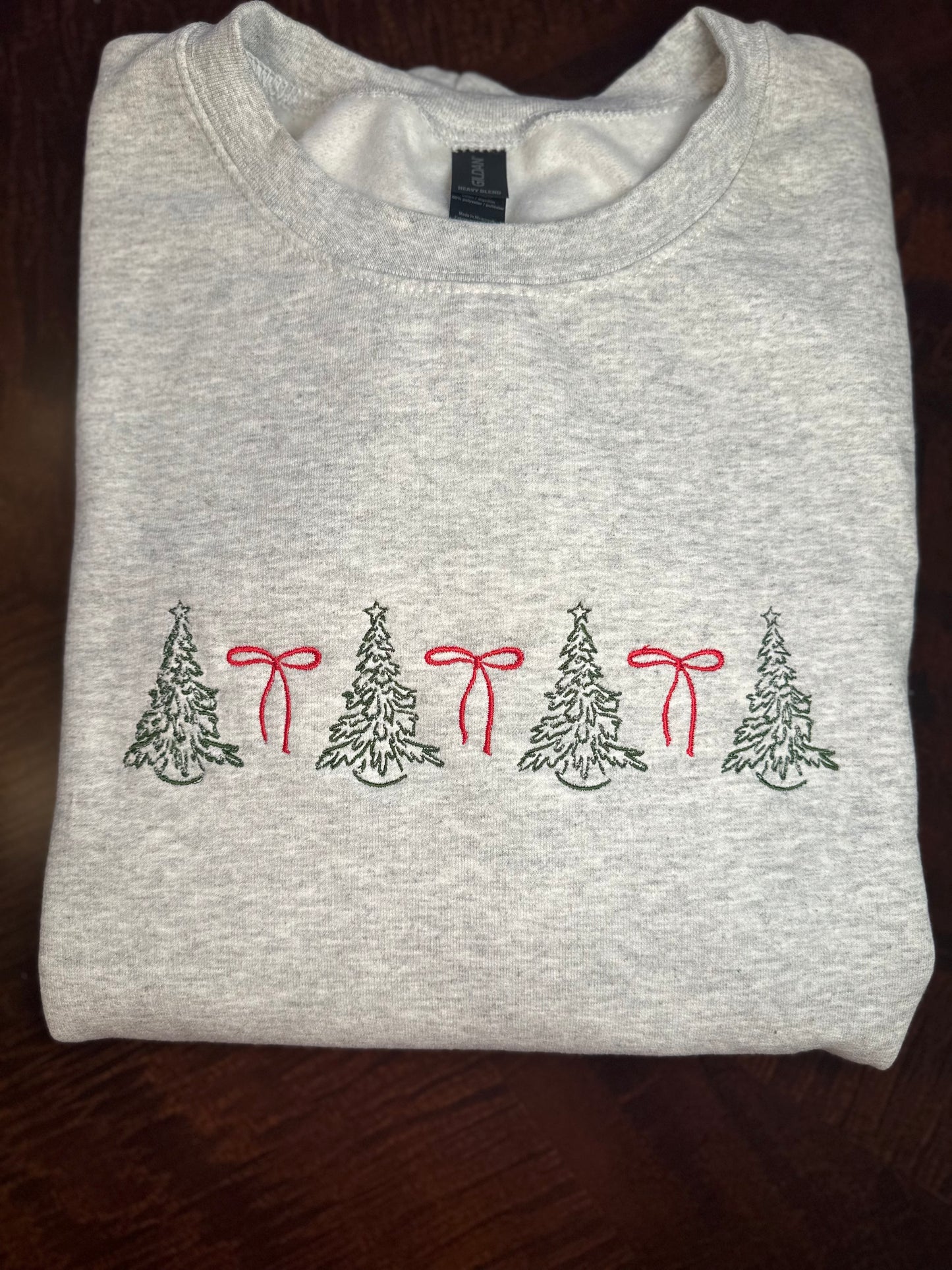 Folded light gray sweatshirt with embroidered green Christmas trees and red bows 