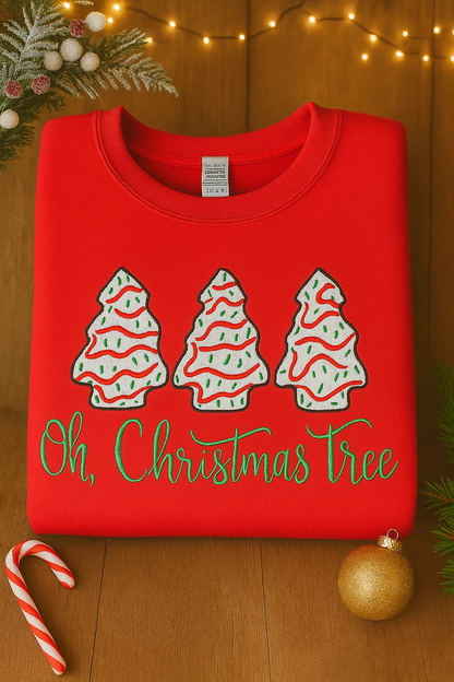 Folded red sweatshirt with embroidered Christmas trees and green “Oh, Christmas Tree” text, styled with festive decorations including lights, candy cane, and gold ornament.