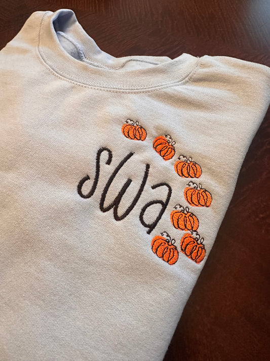 Light blue embroidered crewneck sweatshirt with black monogram letters and small orange pumpkin embroidery frame — personalized fall sweatshirt for women