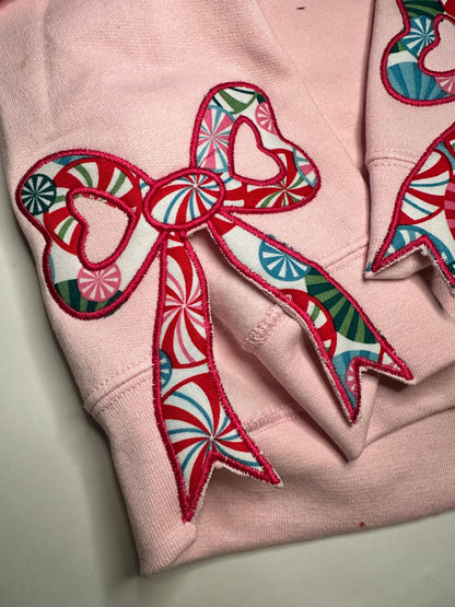 Light pink sweatshirt with festive appliqué bows on the sides, featuring red, green, and blue candy-patterned fabric.