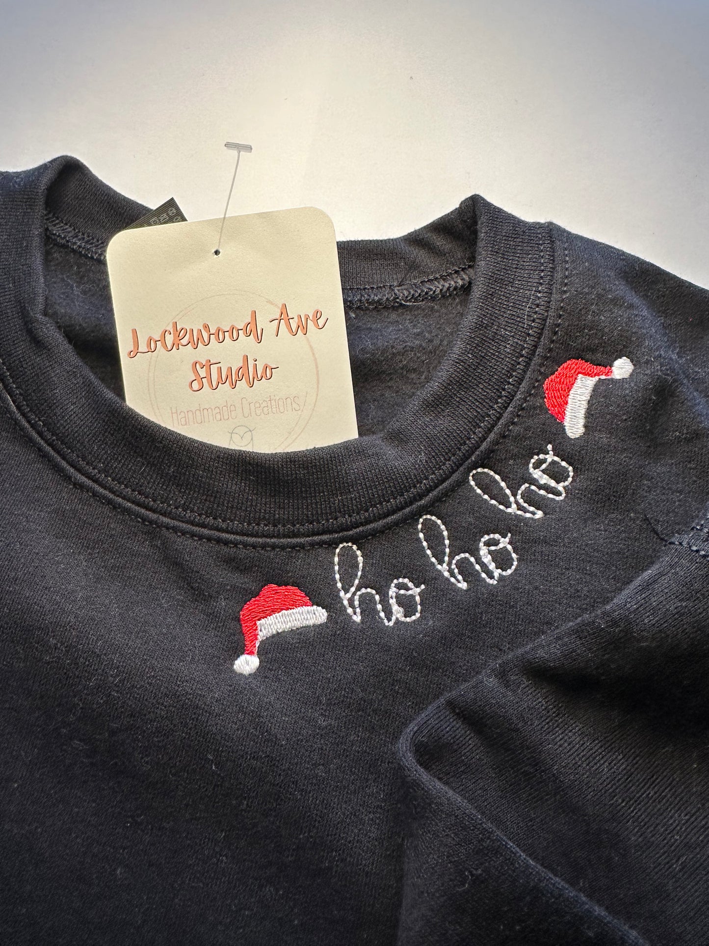 Children’s black sweatshirt featuring “ho ho ho” embroidery with Santa hats on the neckline 