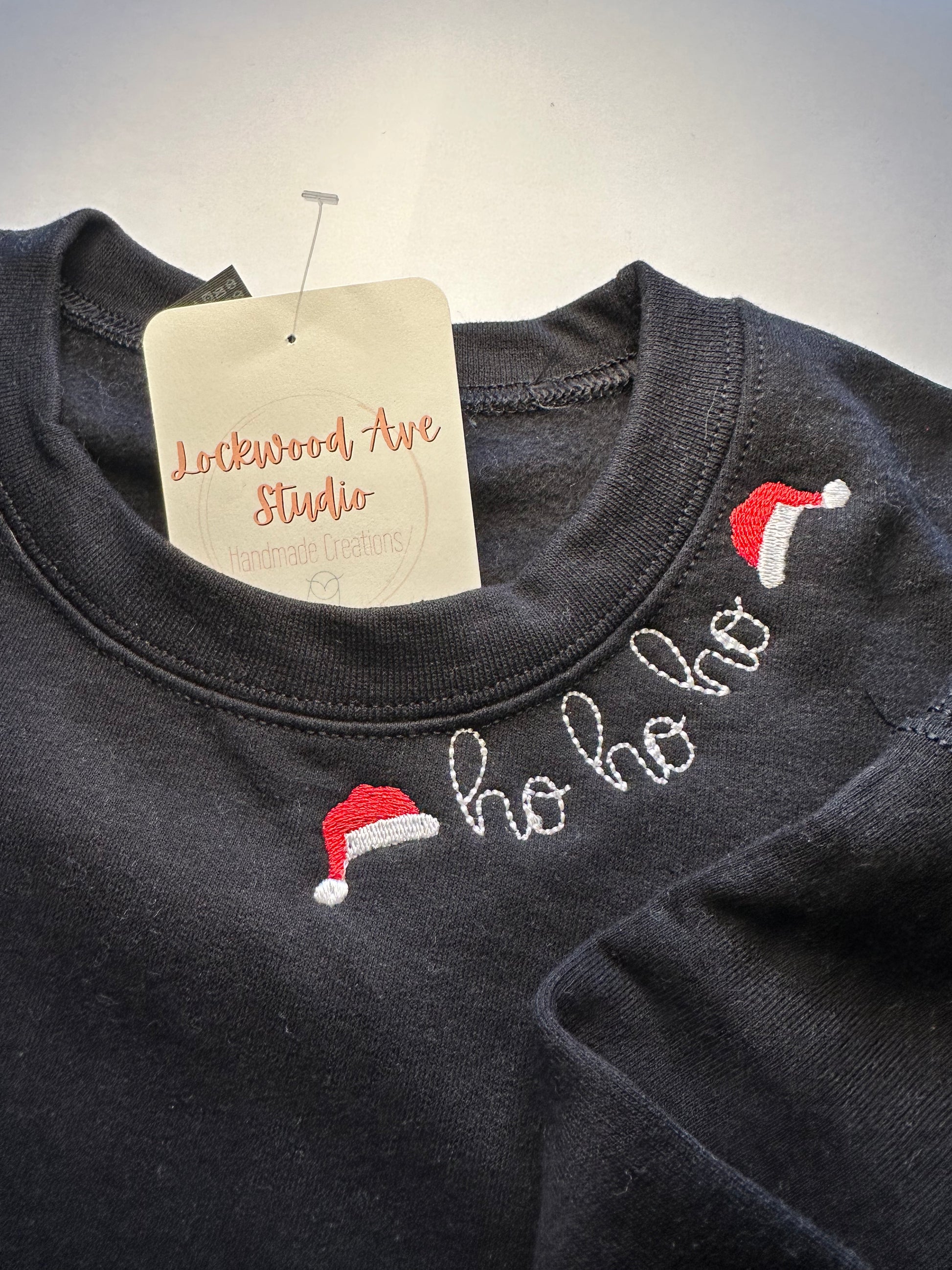 Children’s black sweatshirt featuring “ho ho ho” embroidery with Santa hats on the neckline 