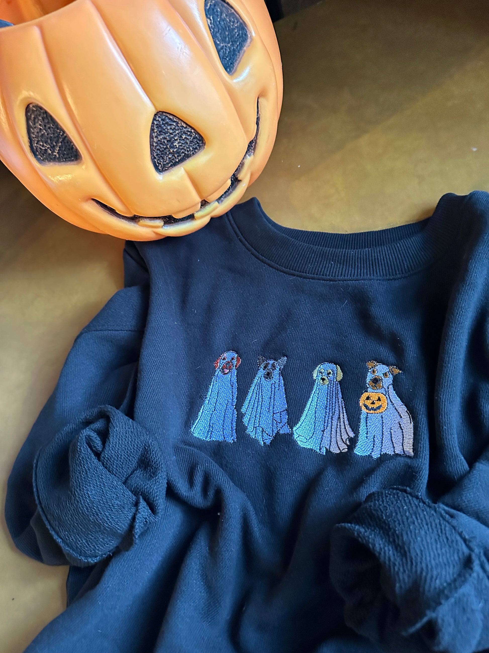 Black sweatshirt with ghost dog design next to a pumpkin on a beige surface