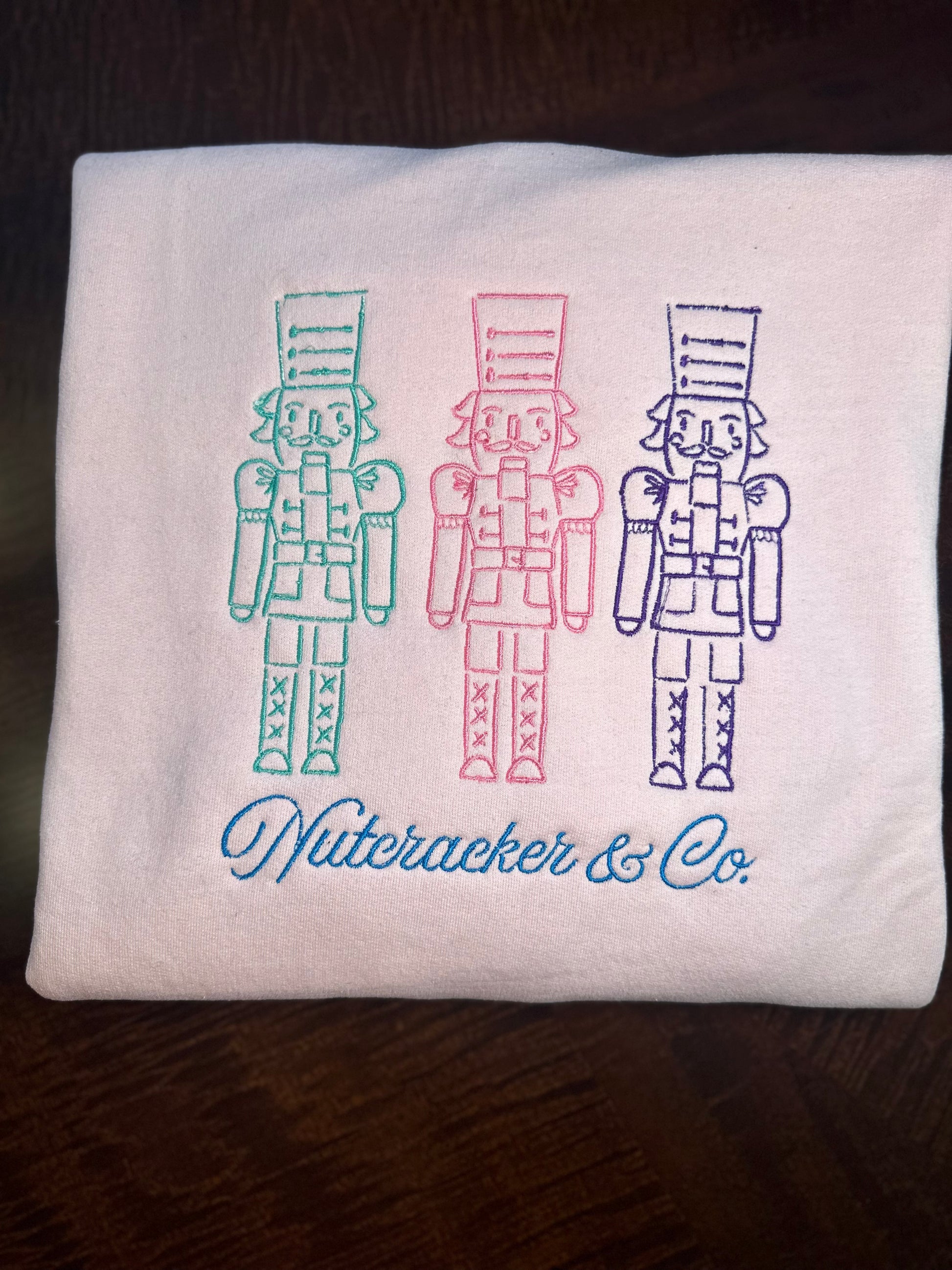 Light Pink embroidered sweatshirts featuring three nutcrackers and “Nutcracker & Co.” script 