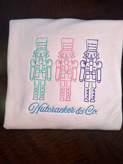 Light Pink embroidered sweatshirts featuring three nutcrackers and “Nutcracker & Co.” script 