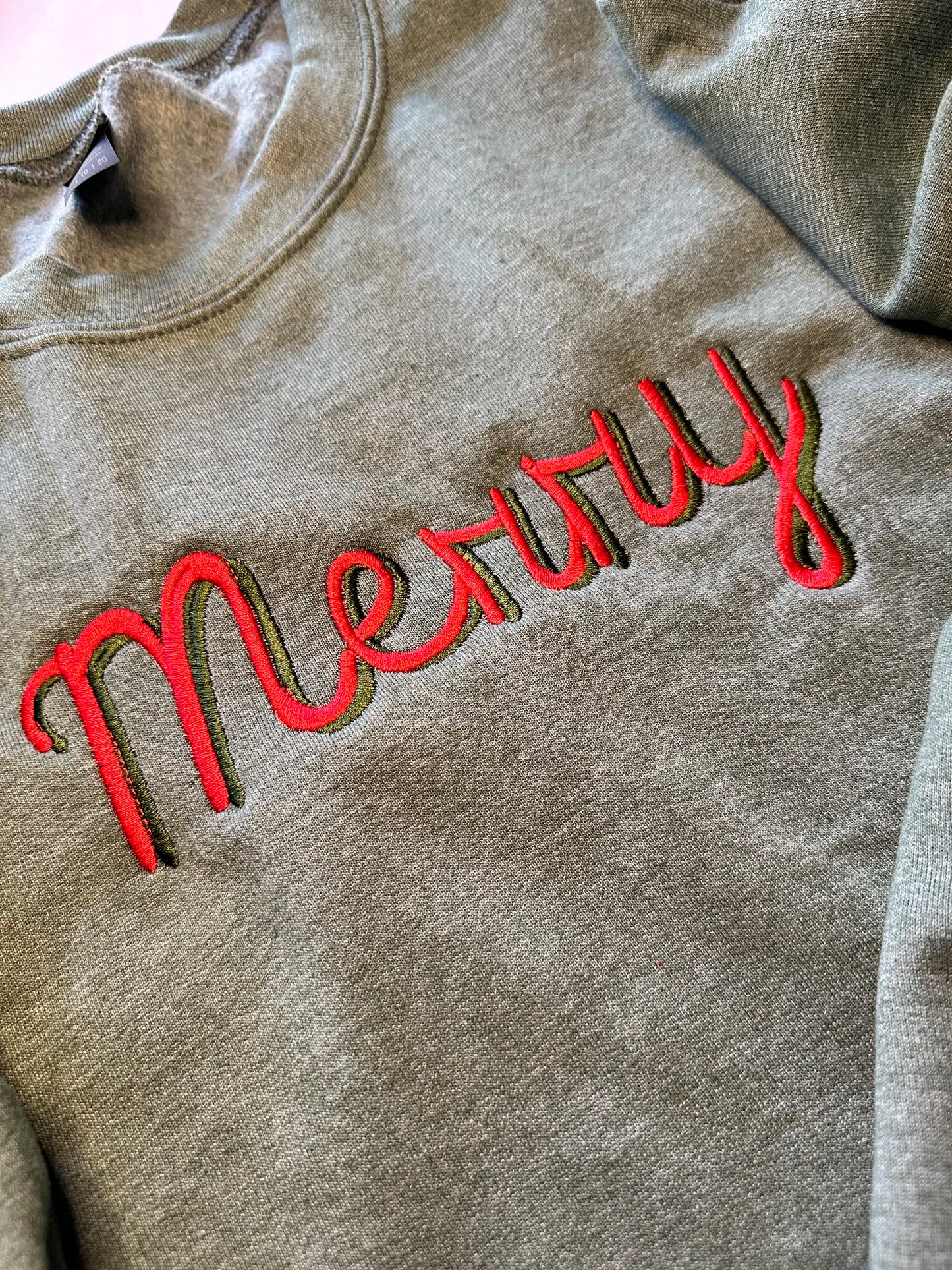 Green sweatshirt with “Merry” embroidered in red and green across the chest 