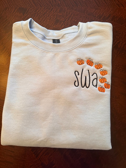 Light blue embroidered crewneck sweatshirt with black monogram letters and small orange pumpkin embroidery frame — personalized fall sweatshirt for women