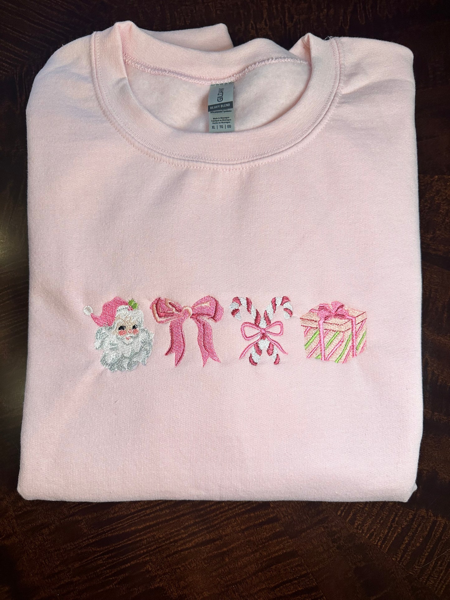 Folded pink sweatshirt with embroidered Christmas icons — Santa, bow, candy canes, and gift box .