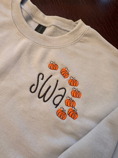 Light blue embroidered crewneck sweatshirt with black monogram letters and small orange pumpkin embroidery frame — personalized fall sweatshirt for women