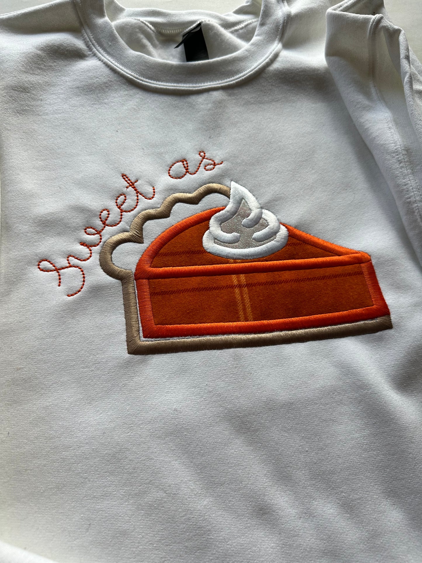 White embroidered crewneck sweatshirt laid flat showing “Sweet as Pie” design with matching pumpkin pie embroidery on waistband