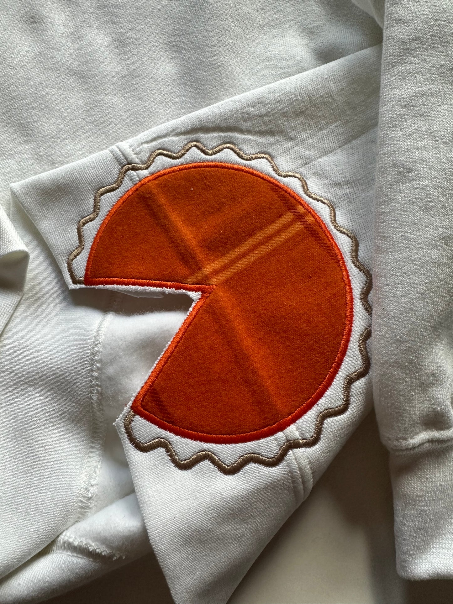White fabric with an orange pie applique patch on a white sweatshirt