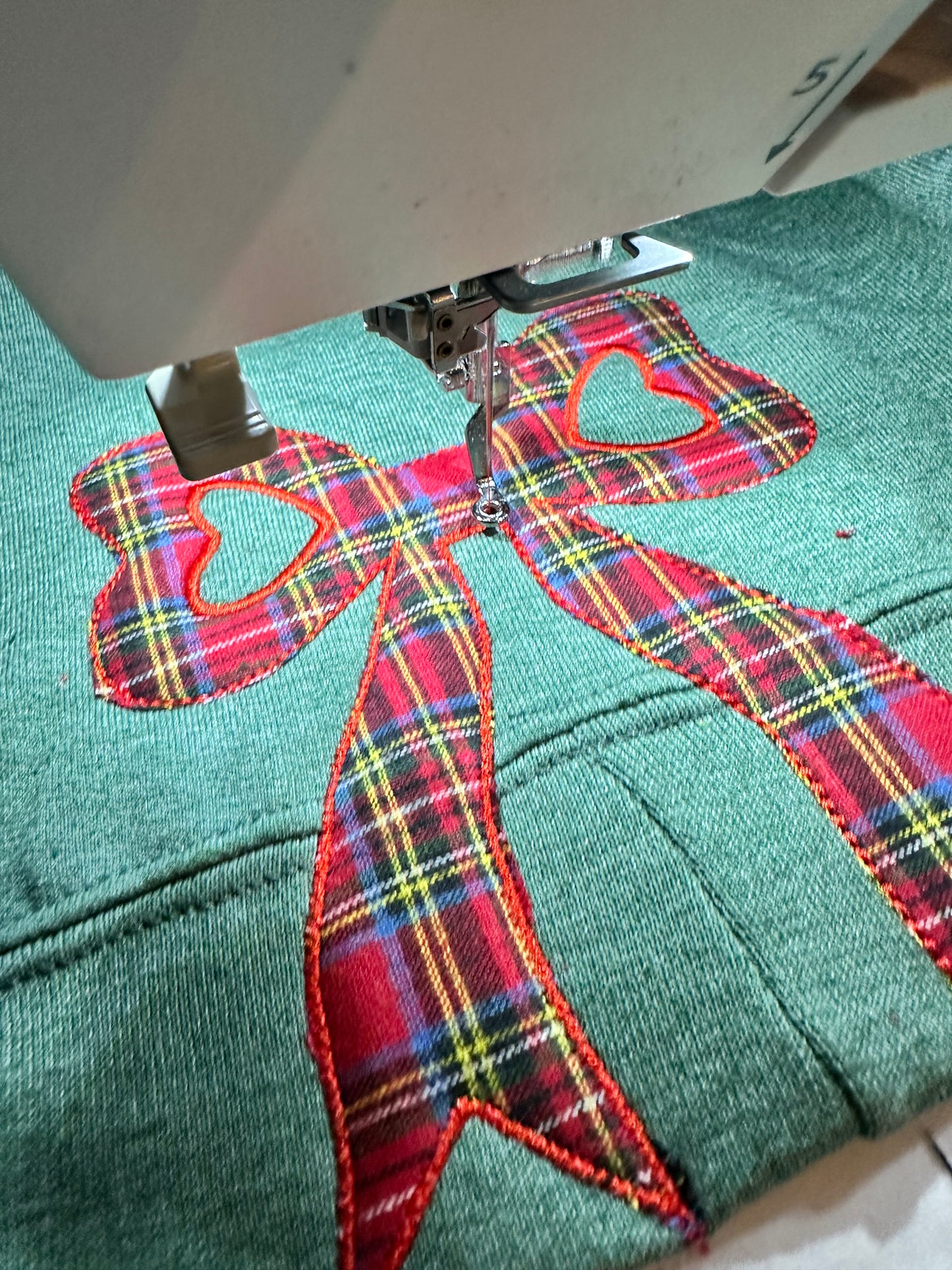 Embroidery machine stitching a red plaid bow design on fabric.