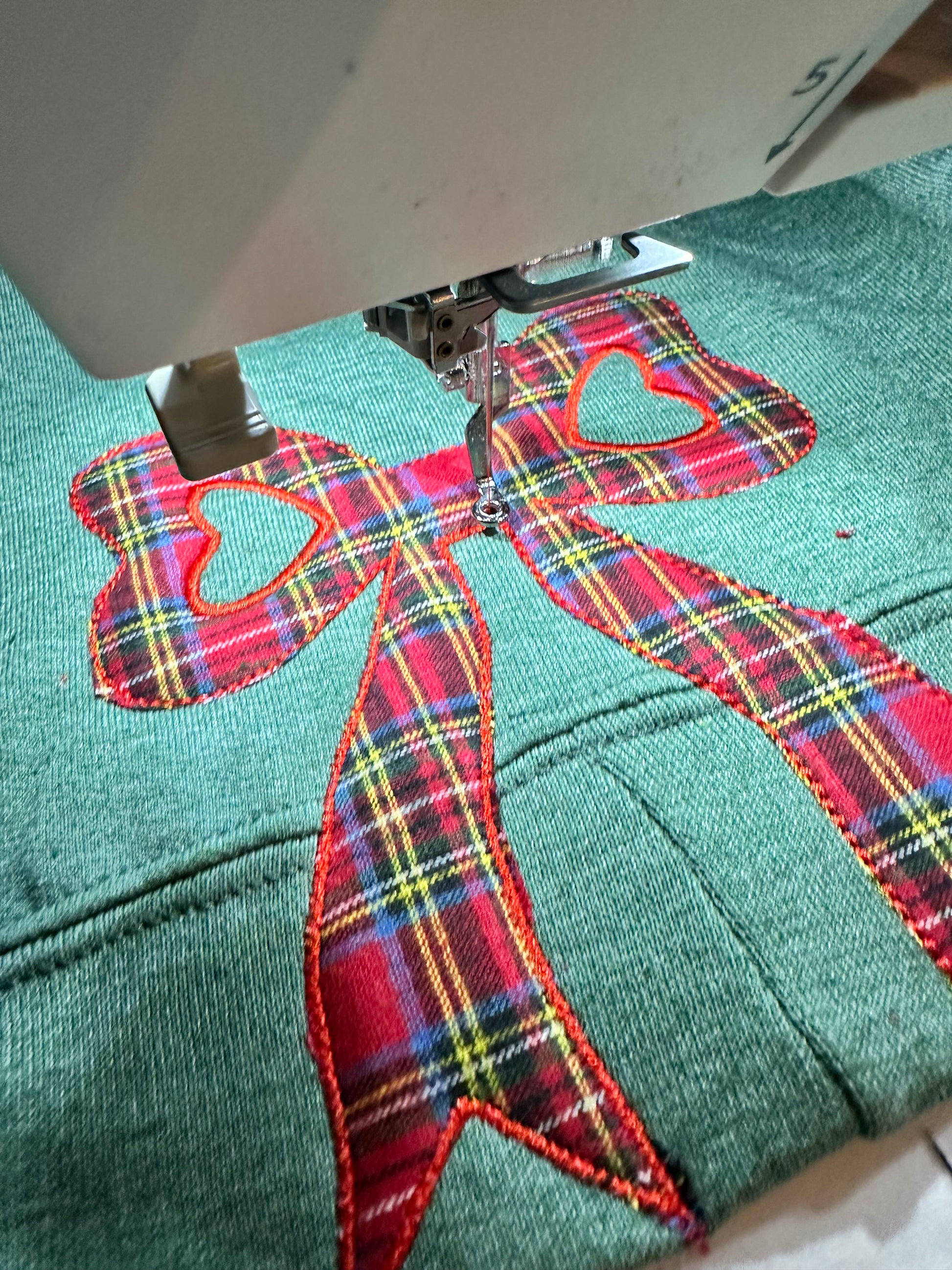 Embroidery machine stitching a red plaid bow design on fabric.