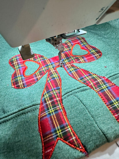 Embroidery machine stitching a red plaid bow design on fabric.