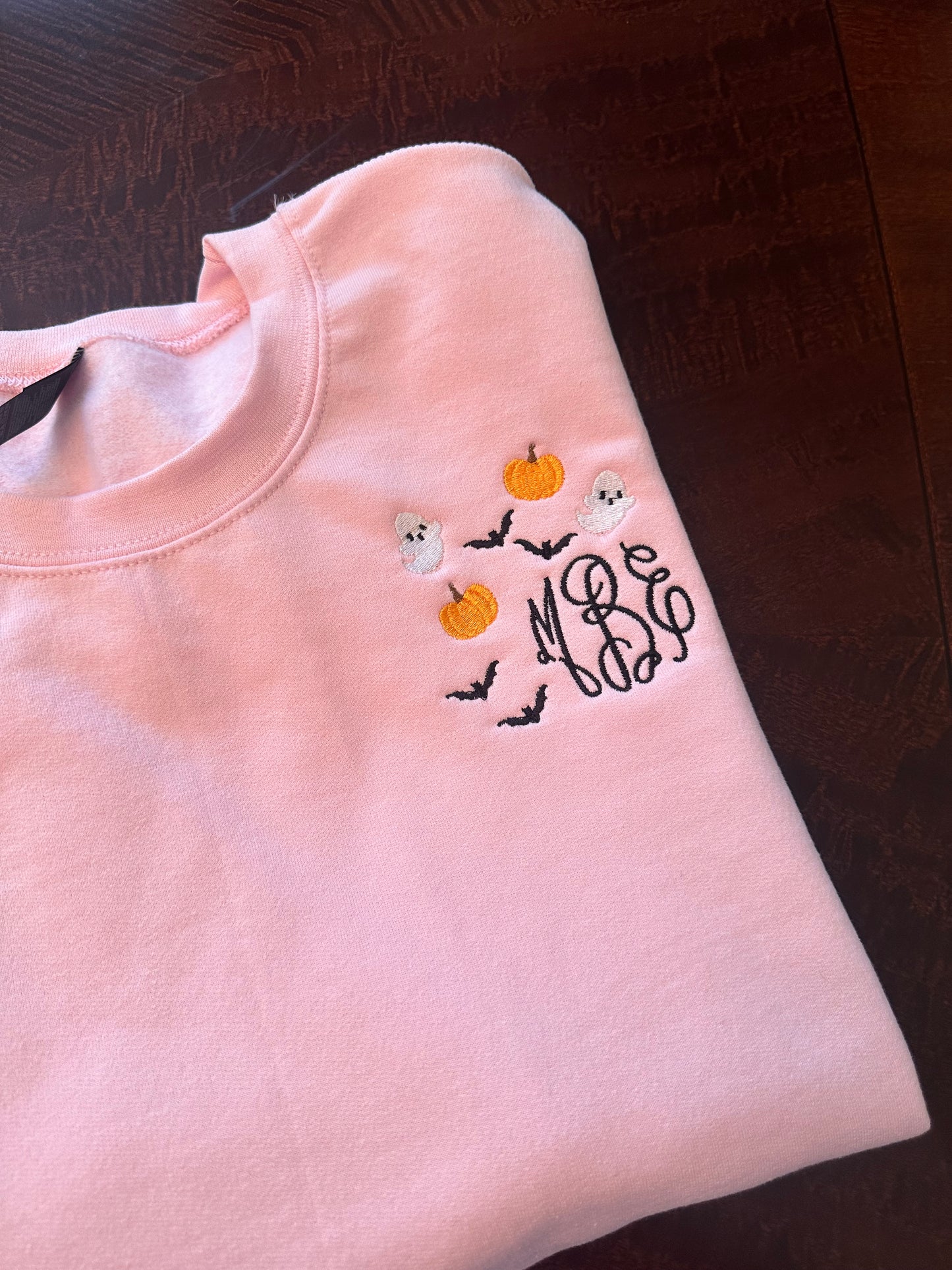Close-up of embroidered Halloween monogram with pumpkins, bats, and ghosts on a pink sweatshirt