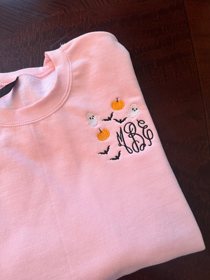Close-up of embroidered Halloween monogram with pumpkins, bats, and ghosts on a pink sweatshirt
