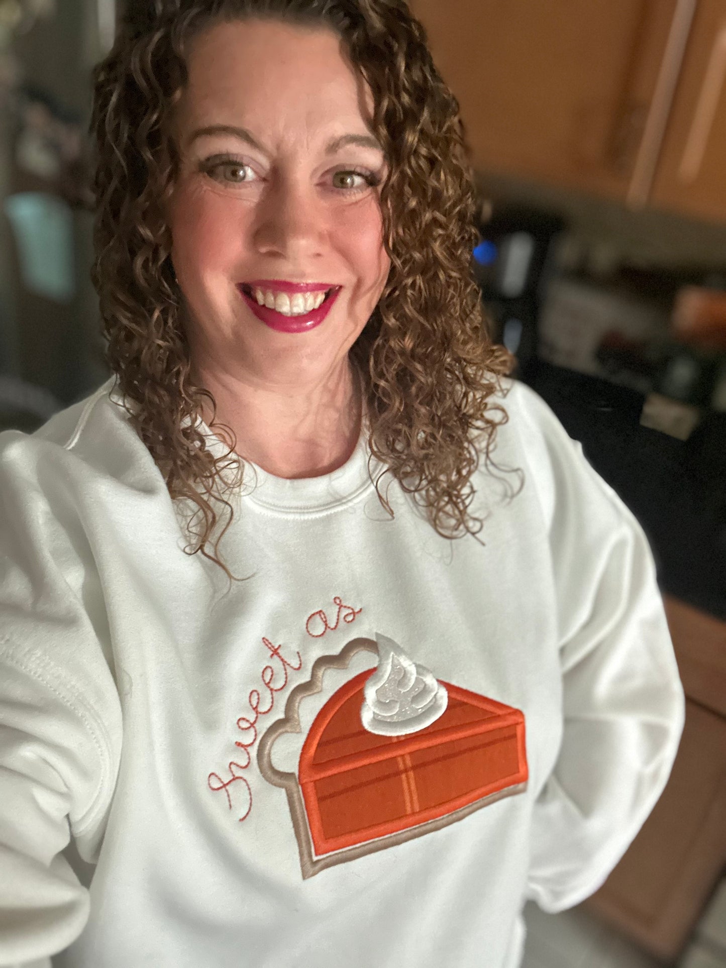 Woman wearing white embroidered sweatshirt with the words “Sweet as Pie” and a pumpkin pie slice design — cozy fall outfit for Thanksgiving