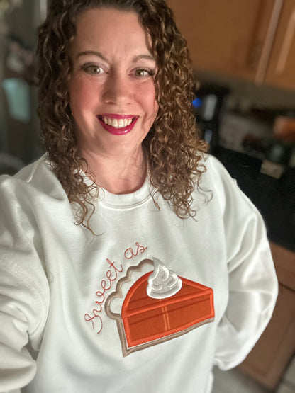 Woman wearing white embroidered sweatshirt with the words “Sweet as Pie” and a pumpkin pie slice design — cozy fall outfit for Thanksgiving