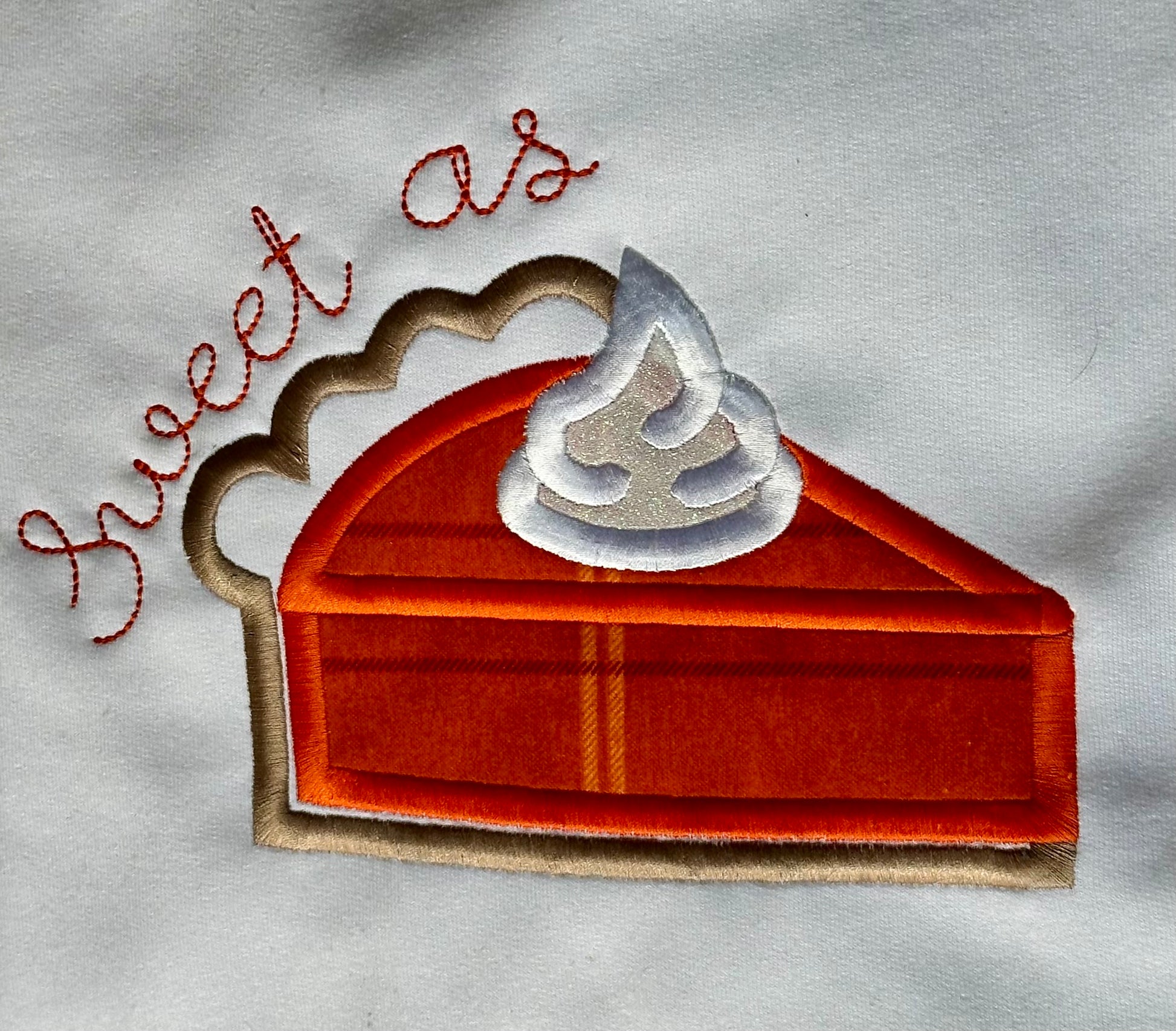 Embroidered patch of a slice of pie with whipped cream and 'sweet as' text on a fabric background